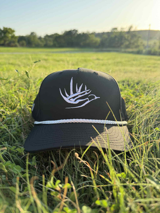 Black Good E Nuff Original hat with white antler-and-bird logo and rope detail placed on grass in outdoor setting