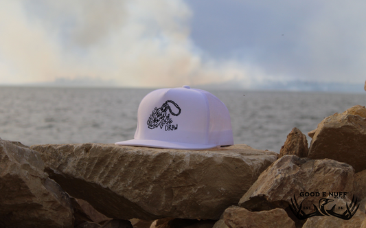 Lucky Rabbit's Foot hat with embroidered design on rocks by the water.