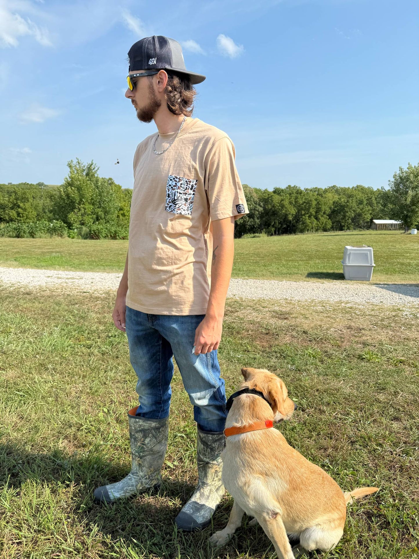 Man wearing Good E Nuff’ Pocket Tee with smoker’s pocket and camo design, standing outdoors with a dog.