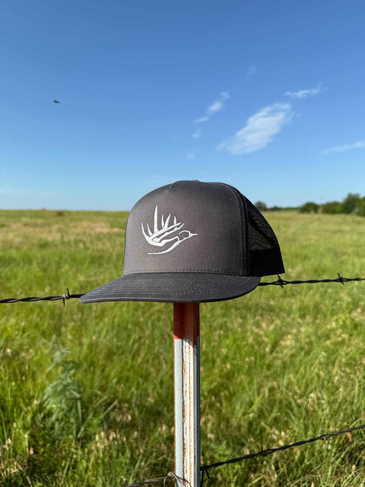 Ridge Flyer black snapback hat with white duck and antlers logo, breathable mesh back, displayed outdoors on a fence post.