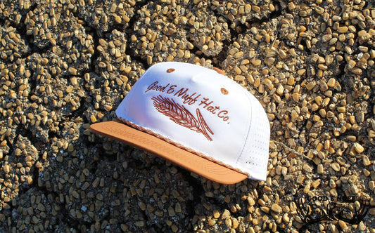 Beer Maker hat with wheat embroidery, white crown, and amber accents on gravel background.